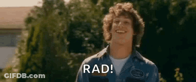A Young Man Is Smiling And Saying `` Rad '' While Standing In Front Of Trees . GIF