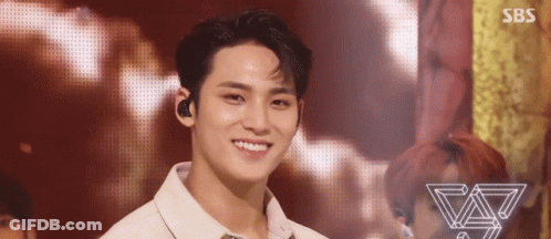 A Young Man Is Smiling On A Stage While Wearing A White Shirt . GIF