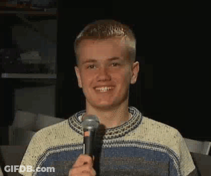 A Young Man Is Smiling While Holding A Microphone In His Hand . GIF