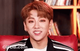 A Young Man Is Smiling While Sitting In A Red Chair . GIF