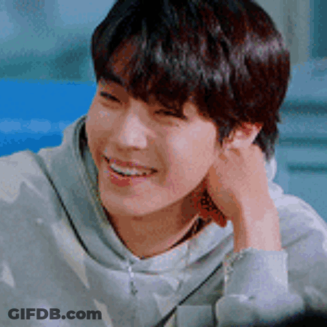A Young Man Is Smiling With His Hand On His Ear And Wearing A Hoodie . GIF
