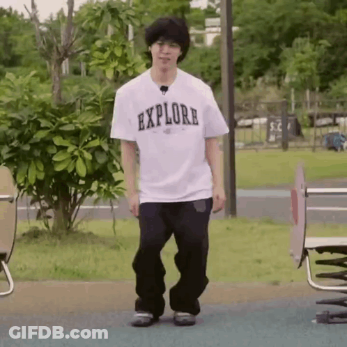 A Young Man Is Standing In A Park Wearing A White T-Shirt That Says Explore . GIF