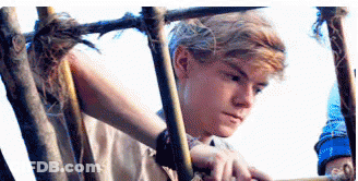 A Young Man Is Standing In A Wooden Cage . GIF
