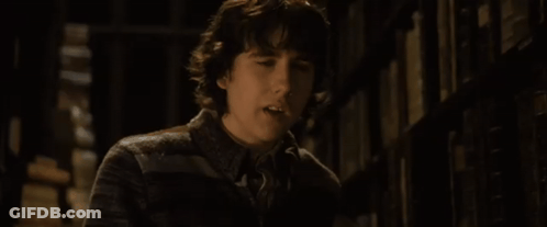 A Young Man Is Standing In Front Of A Bookshelf And Looking At The Camera GIF