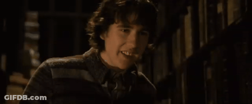 A Young Man Is Standing In Front Of A Bookshelf In A Library . GIF
