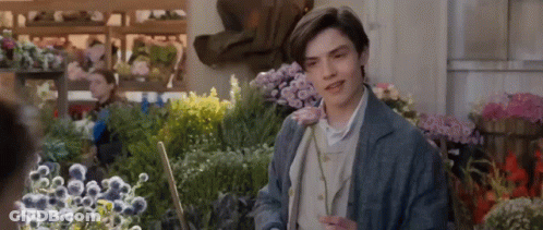 A Young Man Is Standing In Front Of A Bunch Of Flowers In A Flower Shop . GIF