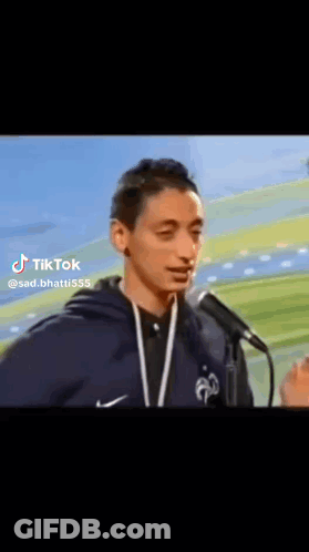 A Young Man Is Standing In Front Of A Microphone And Talking Into It . GIF