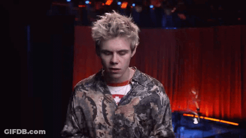 A Young Man Is Standing In Front Of A Red Curtain On A Stage . GIF