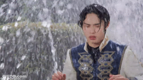 A Young Man Is Standing In Front Of A Waterfall . GIF