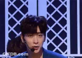 A Young Man Is Standing On A Stage Wearing A Microphone And A Blue Jacket . GIF