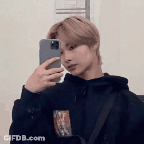 A Young Man Is Taking A Picture Of Himself In A Mirror With His Phone . GIF