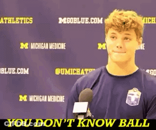 A Young Man Is Talking Into A Microphone In Front Of A Purple Background That Says Michigan Medicine GIF