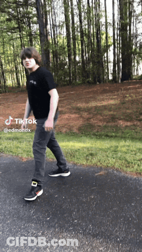 A Young Man Is Walking Down A Road With A Tiktok Sticker On The Bottom GIF