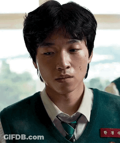 A Young Man Is Wearing A Green Vest And Tie And Has A Name Tag On His Chest . GIF