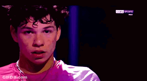 A Young Man Is Wearing A Pink Shirt And A Purple Jacket On A Sports Channel . GIF