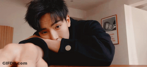 A Young Man Rests His Head On His Arm In Front Of A Framed Picture That Says Oa GIF