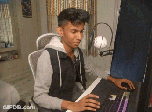 A Young Man Sits At A Desk With A Computer And A Microphone GIF
