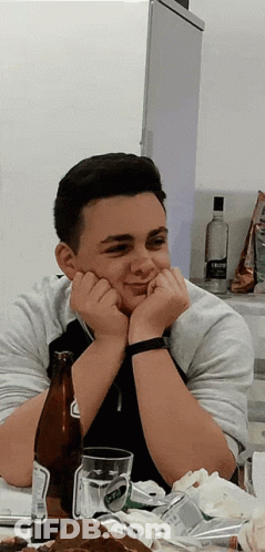 A Young Man Sits At A Table With A Bottle Of Beer And A Glass Of Beer GIF