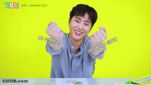 A Young Man Sitting At A Table With His Hands In The Shape Of A Heart And Ybc Written On The Yellow Background GIF