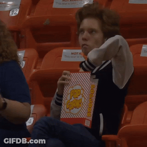 A Young Man Sitting In A Stadium Holding A Box Of Pop Corn GIF