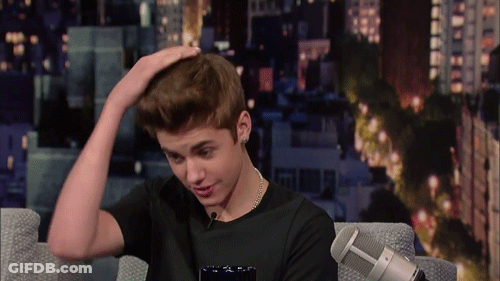 A Young Man Sitting In Front Of A Microphone With His Hand On His Hair GIF