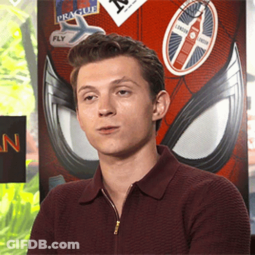 A Young Man Sitting In Front Of A Spider Man Poster With Stickers On It GIF