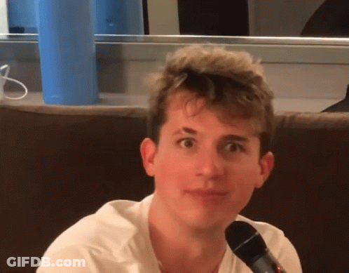 A Young Man Sitting On A Couch With A Microphone GIF