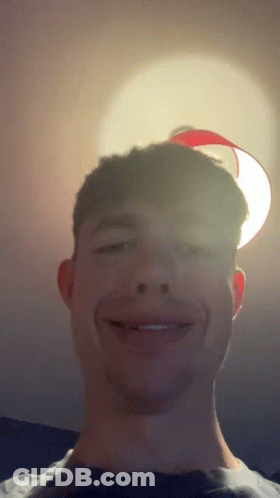A Young Man Smiles In Front Of A Red Lamp GIF