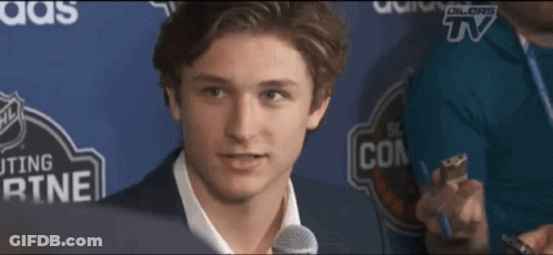 A Young Man Speaking Into A Microphone In Front Of A Sign That Says ' Dillors Tv ' On It GIF