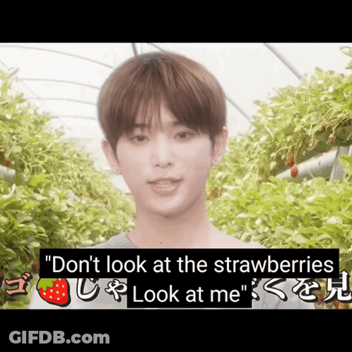 A Young Man Stands In Front Of A Greenhouse With Strawberries Hanging From The Ceiling GIF