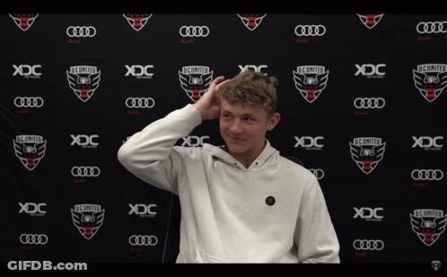 A Young Man Stands In Front Of A Wall That Says Xdc On It GIF