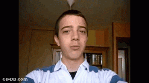 A Young Man Taking A Selfie In A Room With A Bookshelf In The Background GIF