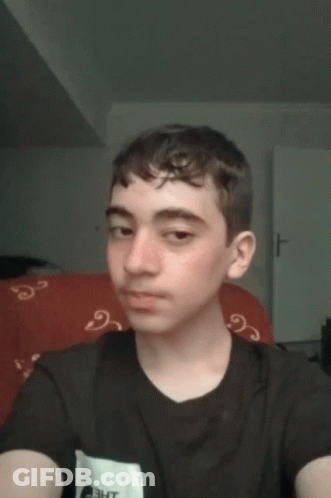 A Young Man Taking A Selfie With A Black Shirt And A Red Couch In The Background GIF