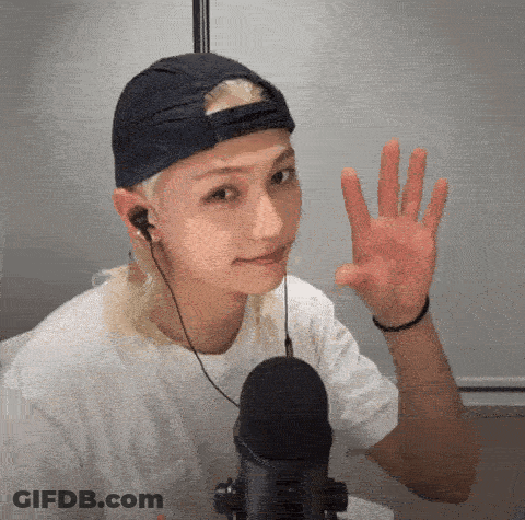 A Young Man Wearing A Baseball Cap And Headphones Is Waving At The Camera . GIF
