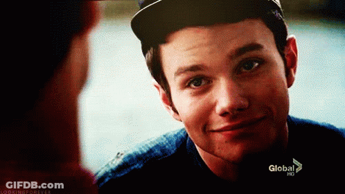 A Young Man Wearing A Baseball Cap Is Smiling And Looking At Another Man . GIF