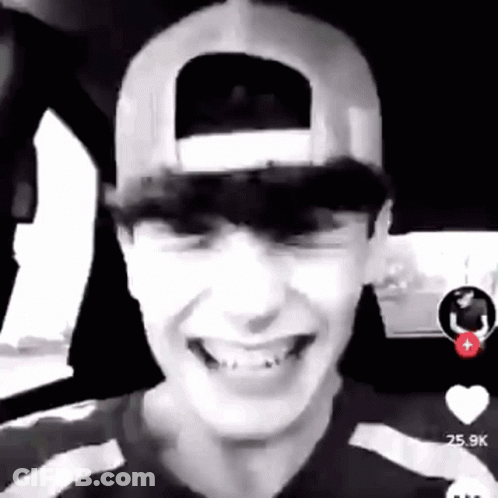 A Young Man Wearing A Baseball Cap Is Smiling In A Car . GIF
