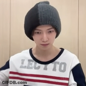 A Young Man Wearing A Beanie And A Striped Shirt Is Standing In Front Of A Wall . GIF