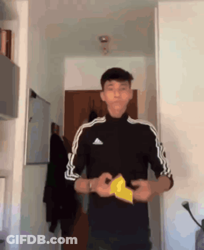 A Young Man Wearing A Black Adidas Shirt Holds A Piece Of Paper In His Hands GIF