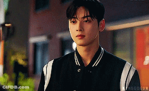 A Young Man Wearing A Black And White Baseball Jacket Is Looking At The Camera . GIF