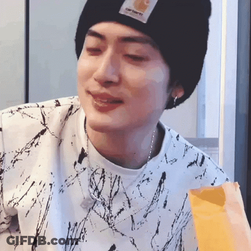 A Young Man Wearing A Black Beanie And A White Shirt Is Eating A Bag Of French Fries . GIF
