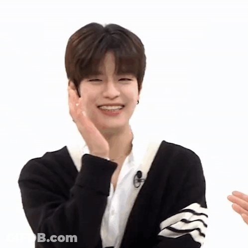 A Young Man Wearing A Black Cardigan And A White Shirt Is Smiling While Holding His Hand To His Face . GIF