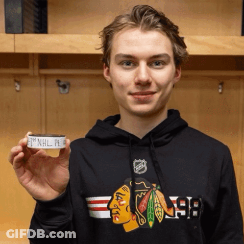 A Young Man Wearing A Black Chicago Blackhawks Sweatshirt Is Holding A Hockey Puck GIF