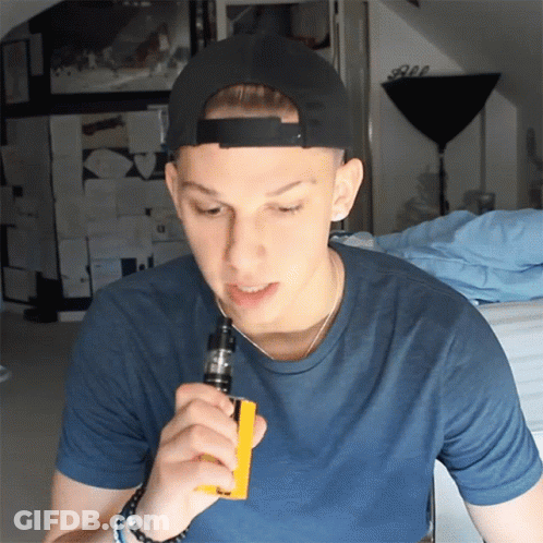 A Young Man Wearing A Black Hat And A Blue Shirt Smoking An Electronic Cigarette GIF