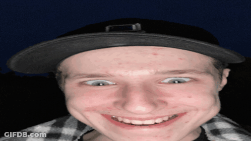 A Young Man Wearing A Black Hat And Plaid Shirt Smiles For The Camera GIF