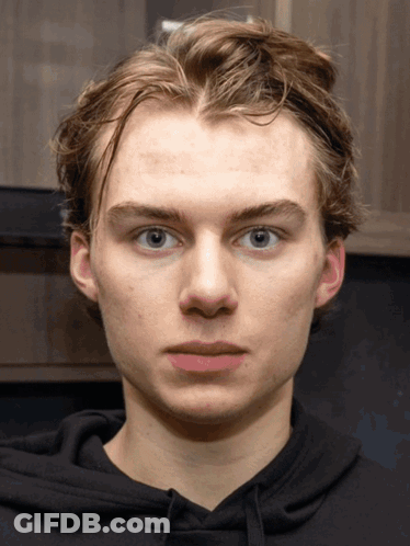 A Young Man Wearing A Black Hoodie Looks At The Camera With A Serious Look On His Face GIF