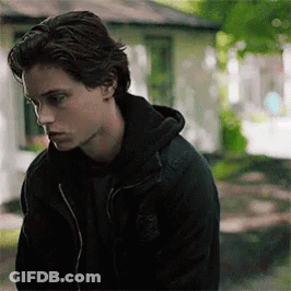 A Young Man Wearing A Black Jacket And A Black Hoodie Is Standing In Front Of A House . GIF