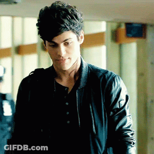 A Young Man Wearing A Black Leather Jacket And A Black Shirt Is Standing In A Hallway . GIF