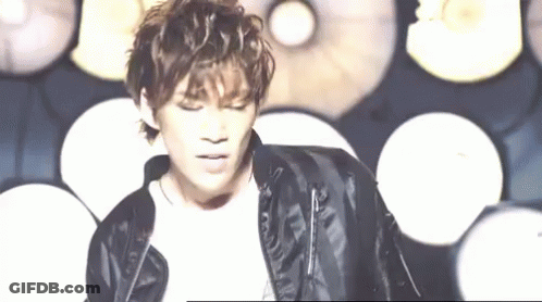 A Young Man Wearing A Black Leather Jacket Is Standing In Front Of A Wall Of Lights . GIF