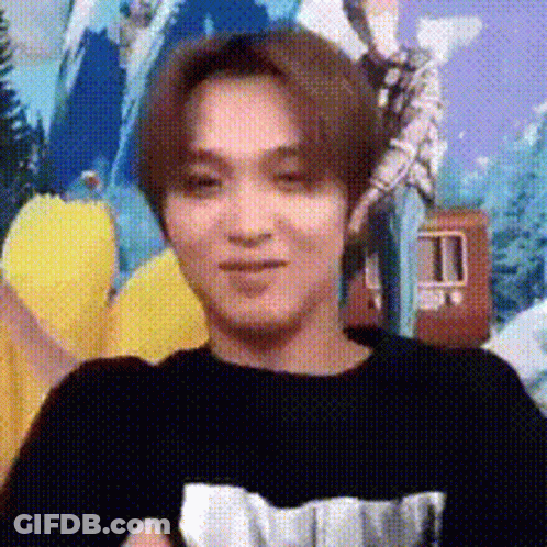A Young Man Wearing A Black Shirt Is Sitting In Front Of A Wall With A Picture On It . GIF