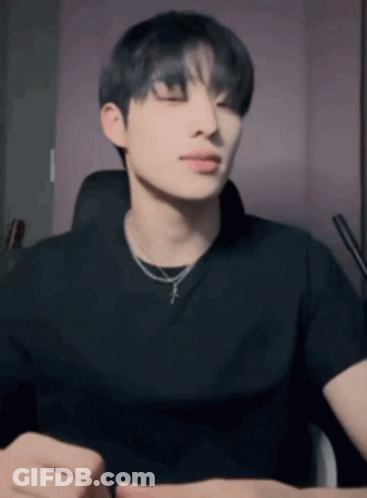 A Young Man Wearing A Black T-Shirt And A Necklace Is Sitting In A Chair With His Eyes Closed . GIF